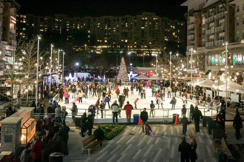Pentagon row ice skating rink, full of people with a Christmas tree and light